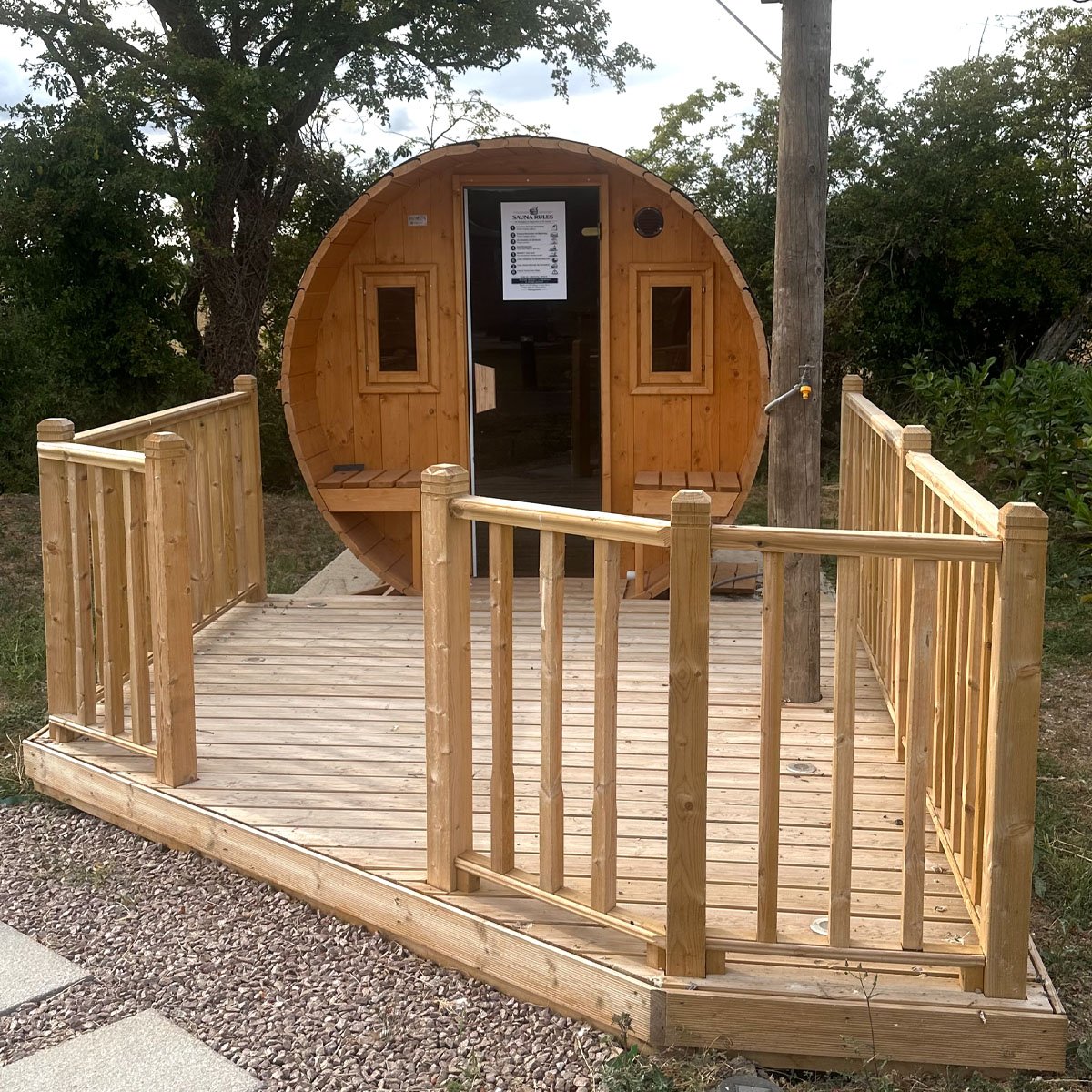 The barrel sauna on its raised timber deck, with the door standing open
